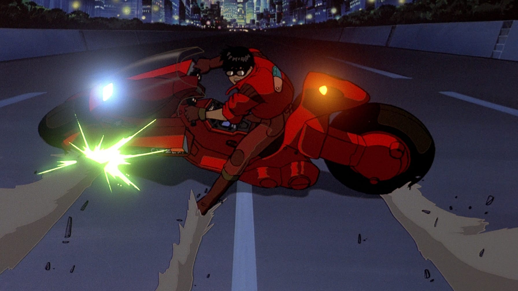 Screencap from the movie AKIRA that shows a young man in red motorcycle gear. He is sliding on a red motorbike on the highway of a futuristic city at night.