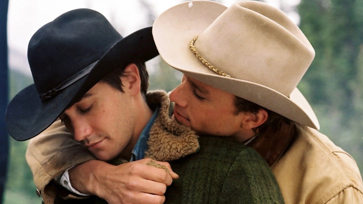 Screencap from the movie Bbrokeback Mountain showing two men wearing cowboy hats and ranger gear looking outside of the frame.